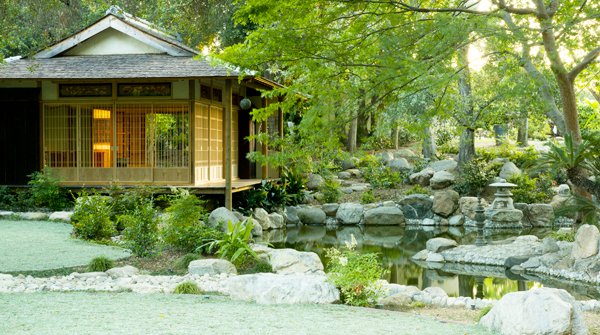 Traditional Japanese teahouse glowing at dusk beside a rock-lined pond at Storrier Stearns Japanese Garden in Pasadena