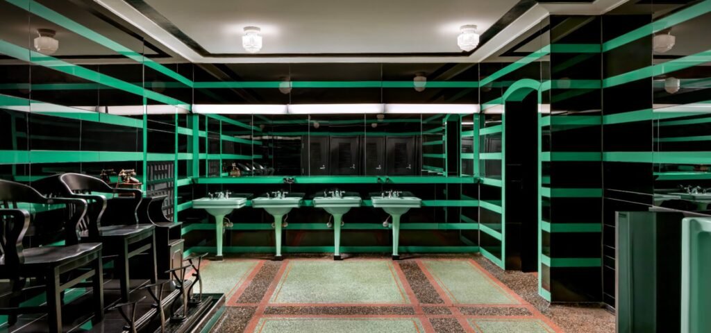 Wide view of the Hermitage Hotel’s iconic green-striped Art Deco men’s bathroom with pedestal sinks and terrazzo floor.