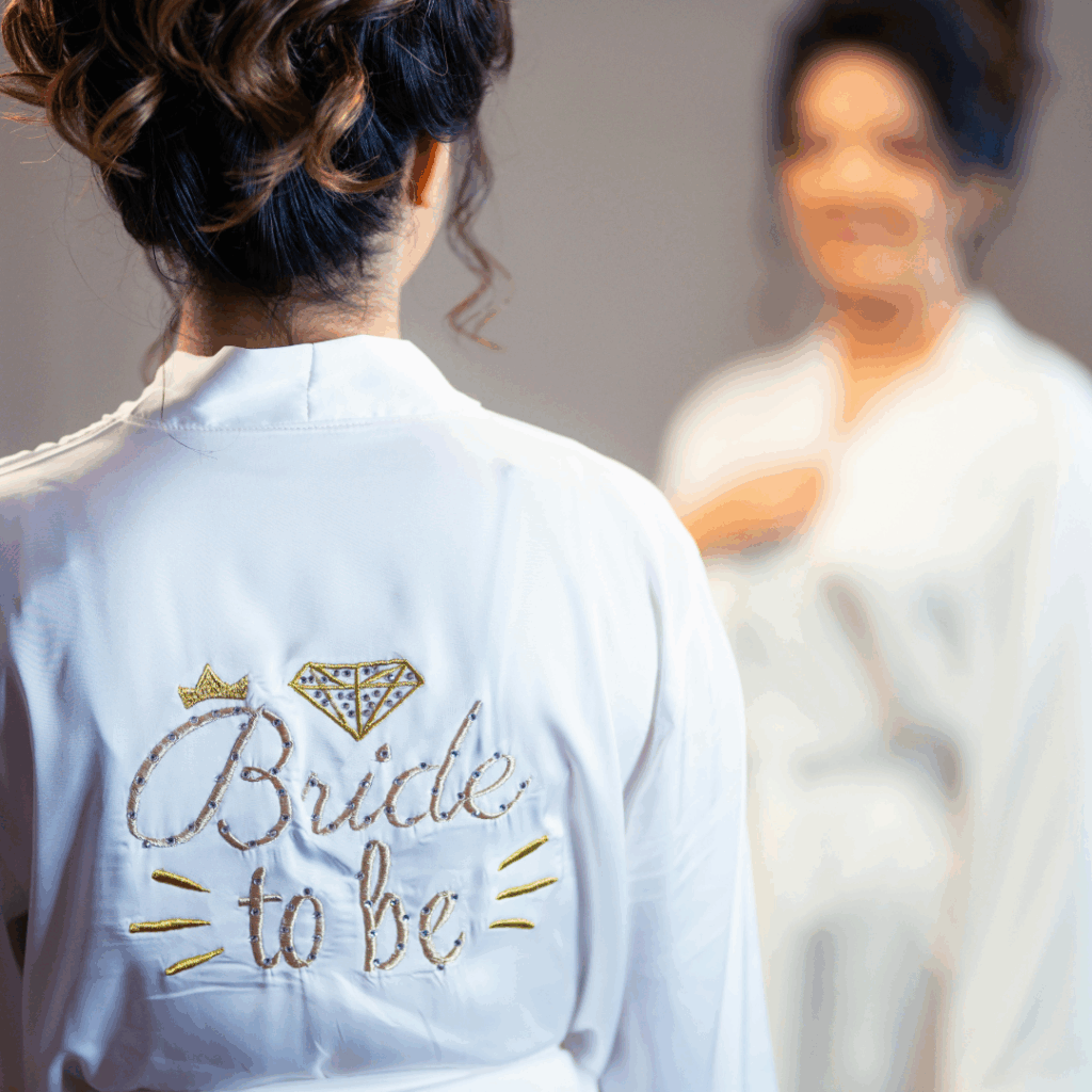 Bride-to-be wearing a white satin “Bride to Be” robe while getting ready—an item from the wedding morning essentials checklist.