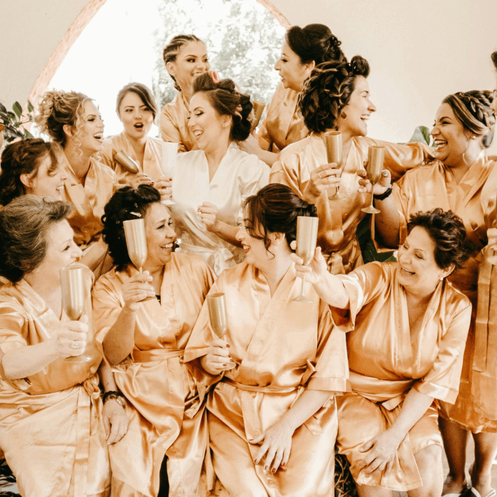 Bride and her bridal party in matching gold satin robes raising gold champagne flutes in a joyful toast