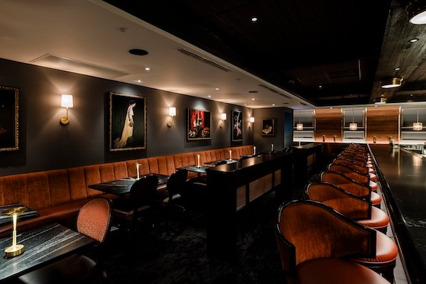 Elegant, dimly lit lounge with burnt-orange banquette seating, portrait art, and a long marble bar at Bern’s Steak House in Tampa