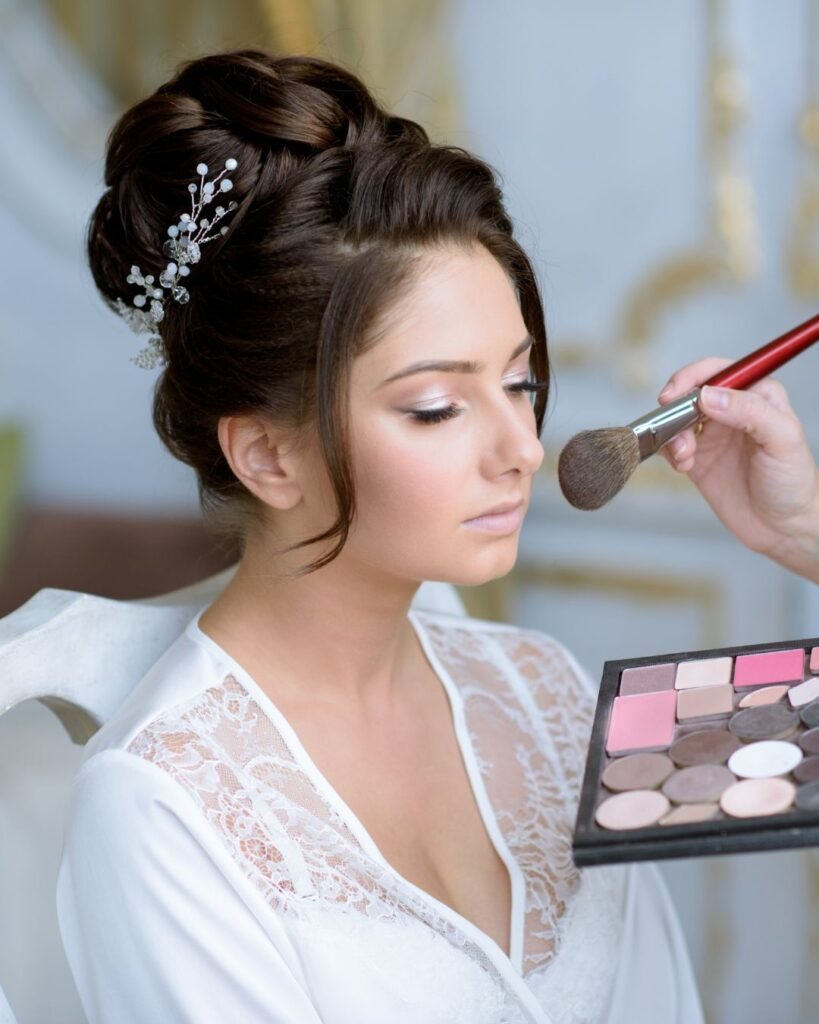 Bride getting makeup done with soft pink tones, featuring elegant updo hairstyle with pearl hairpin — perfect wedding hair and makeup inspiration