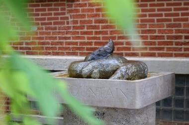 Shit Fountain Chicago bronze poop fountain framed by green leaves, set against a red-brick wall