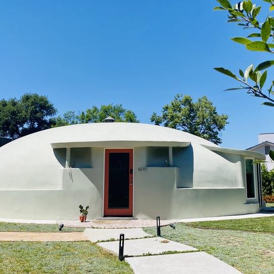 Renovated Bubble House Pasadena with smooth dome and orange-trimmed door under a clear blue sky