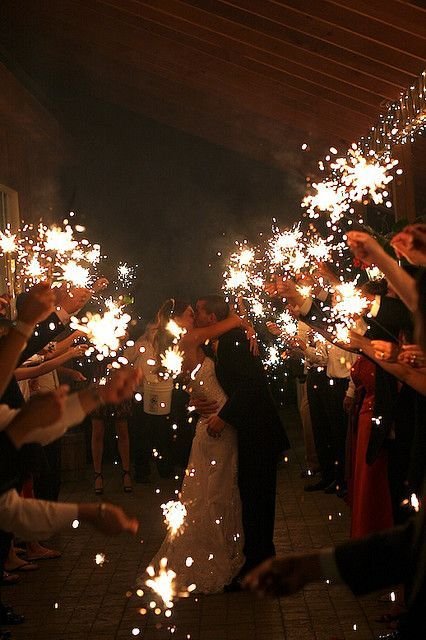 Bride and groom kissing during sparkler wedding exit surrounded by guests.
