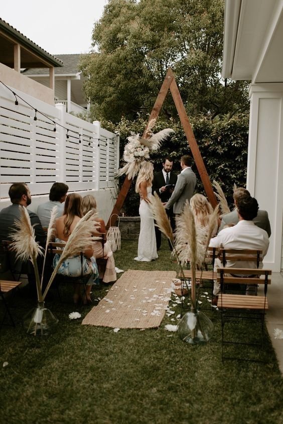 Intimate backyard micro wedding ceremony with rustic triangle arch and pampas grass décor.