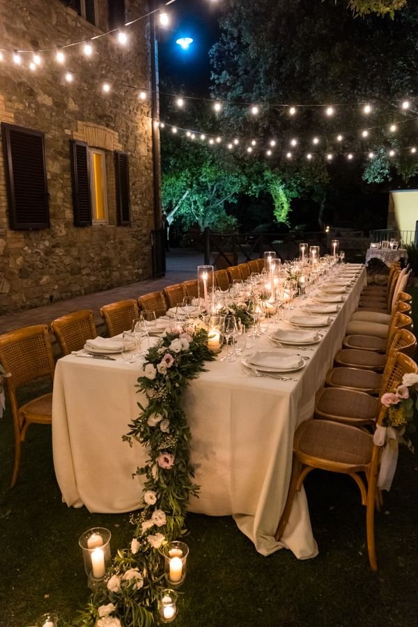 Long dinner table set for a micro wedding reception with string lights and floral décor.