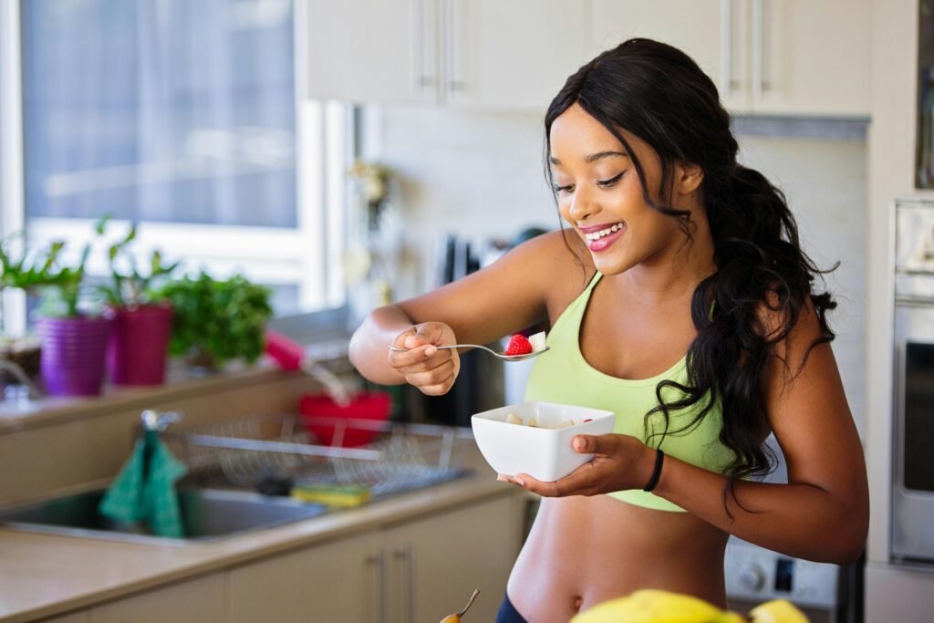 Smiling woman in sportswear eating a fresh fruit bowl in the kitchen