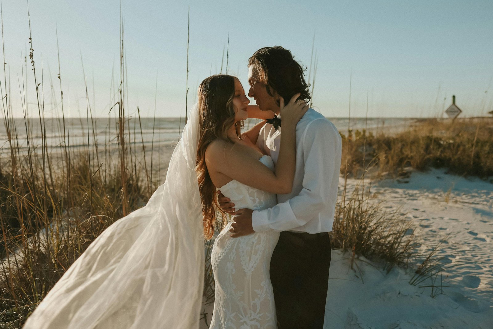 Romantic beach wedding couple embracing on the sand dunes during sunset in Florida.