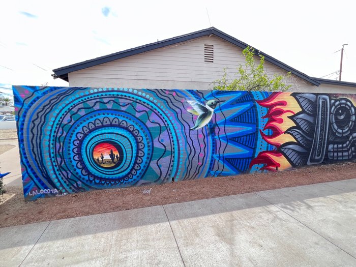 Vibrant mural by artist Lalo Cota with a hummingbird, desert sunset, and bold circular designs at Oak Street Alley in Phoenix, Arizona.