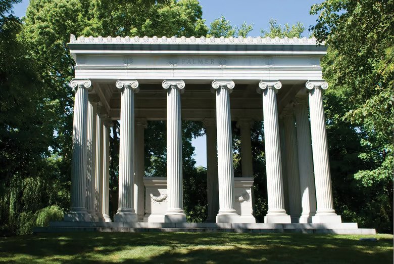 Classical mausoleum with tall columns and trees reflected in the lake at Graceland Cemetery in Chicago, Illinois.