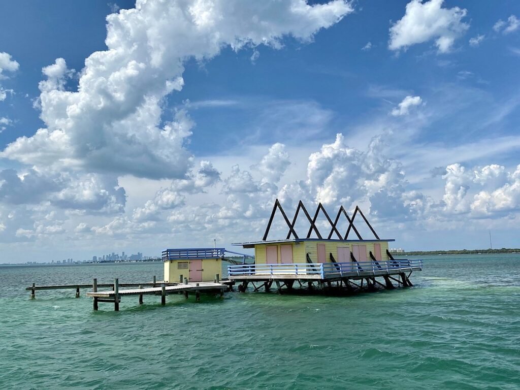 Colorful Stiltsville house on stilts in Biscayne Bay with Miami skyline in the distance.