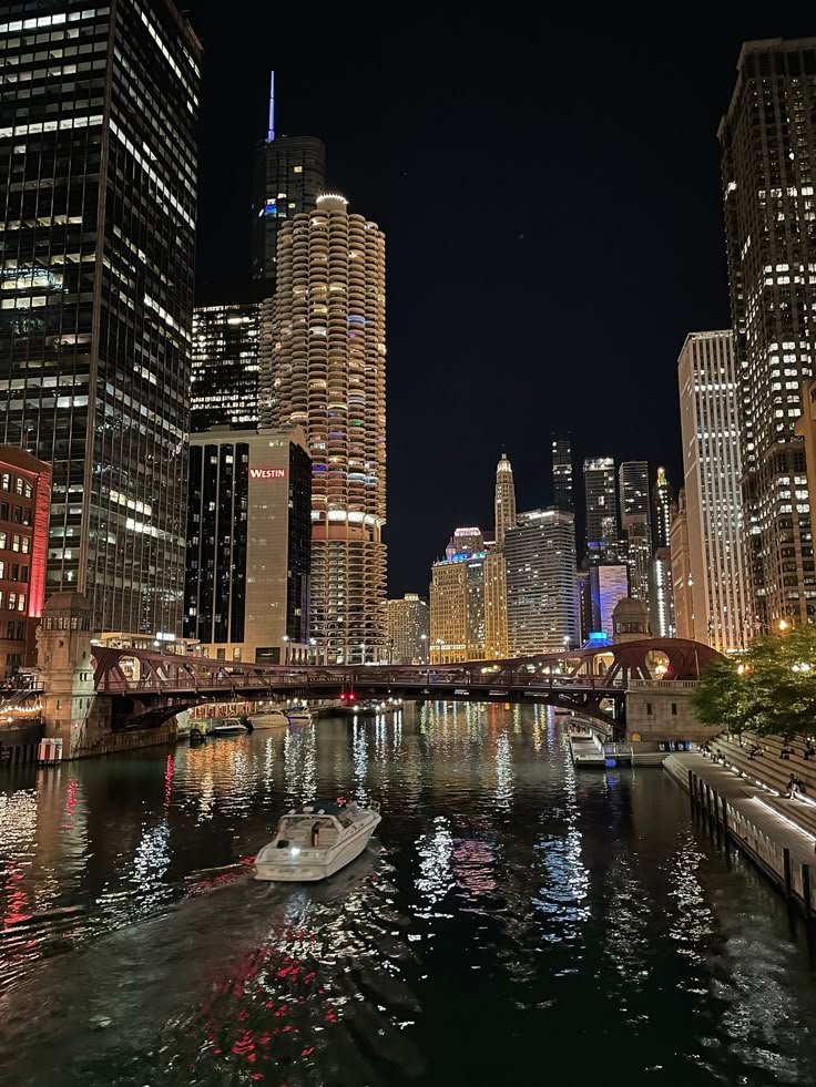 Boat cruising along the Chicago River at night surrounded by city skyscrapers and reflections of lights on the water.