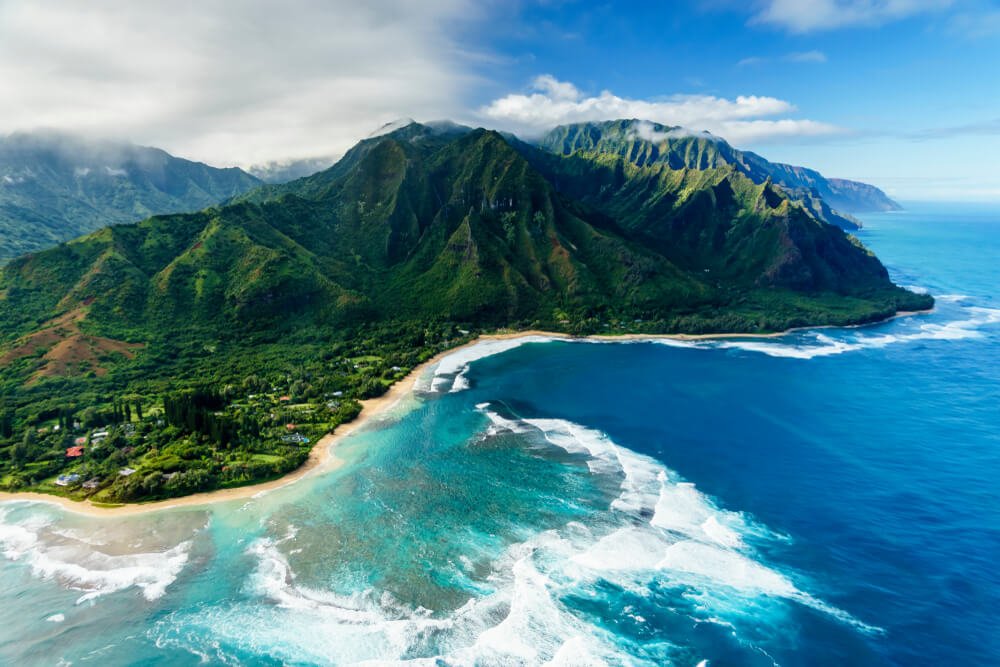 Aerial view of the lush Nā Pali Coast cliffs and ocean waves on Kauaʻi, Hawaii.