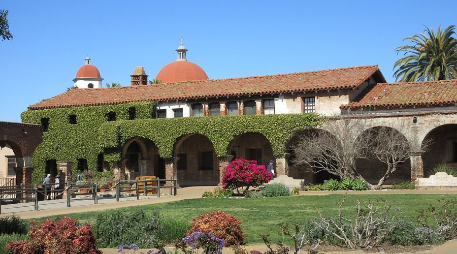 Historic Mission San Juan Capistrano with ivy-covered walls and red domes under blue skies.