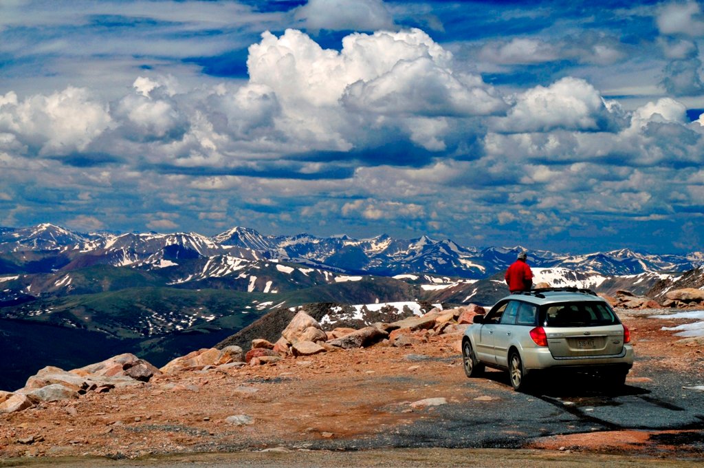 Car parked at the summit of Mount Blue Sky overlooking snow-covered peaks in Colorado.