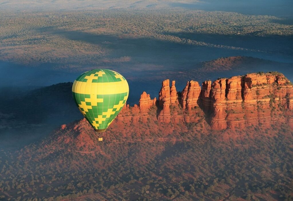 Group of travelers riding a red and yellow hot air balloon above Sedona’s red cliffs.