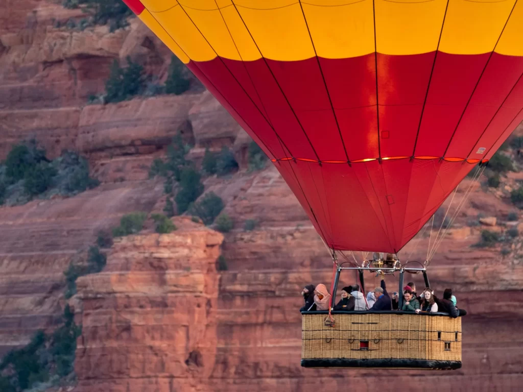 Yellow and green hot air balloon floating above Sedona red rock formations at sunrise.