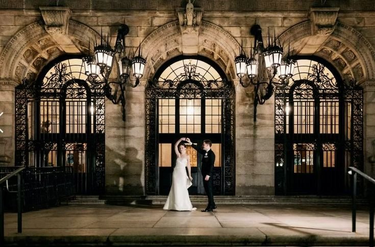 Bride and groom dancing outside Boston Public Library under classic iron archways at night.