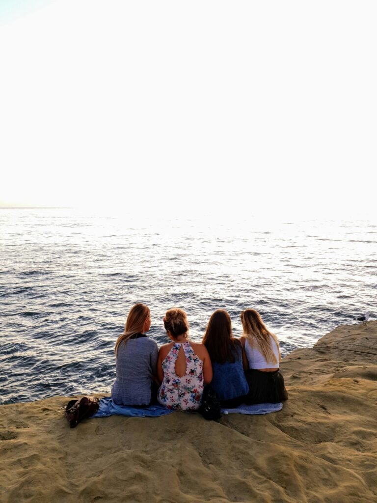 Four women sitting on a cliff at sunset overlooking the ocean in San Diego, enjoying a peaceful family moment by the water.