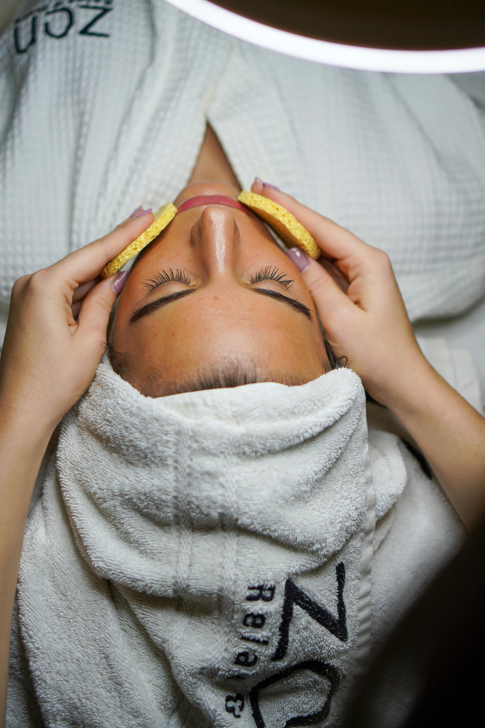 Woman enjoying a relaxing facial treatment at a wellness day spa in Los Angeles, wearing a white robe and towel wrap.