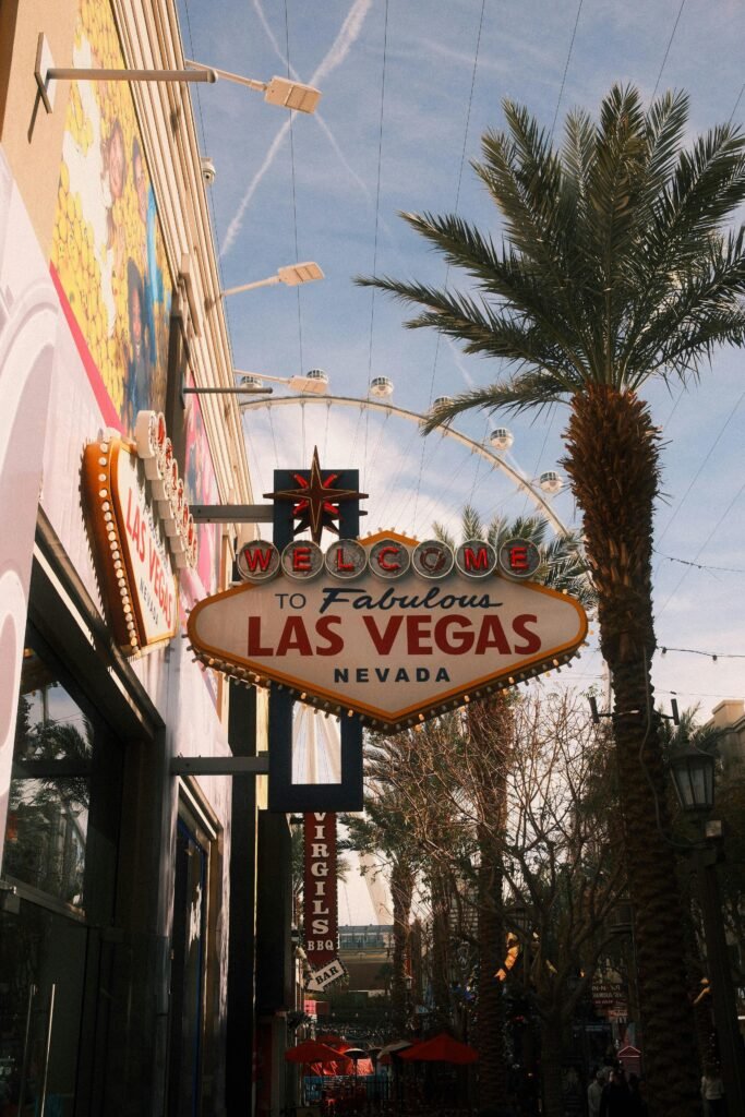 Welcome to Fabulous Las Vegas” sign surrounded by palm trees and nearby shops on a sunny day.