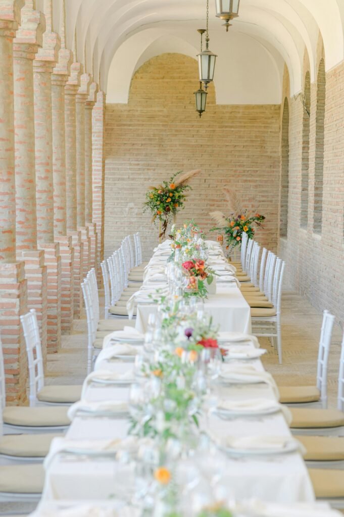 Elegant outdoor wedding reception setup in Malibu with long banquet tables, white chairs, and floral centerpieces under brick arches.