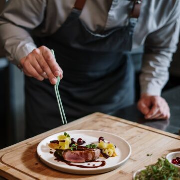 person holding fork and knife slicing vegetable on white ceramic plate
