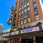 Iconic exterior of Tampa Theatre in Tampa Florida with its vintage marquee and bold vertical sign under a clear blue sky.