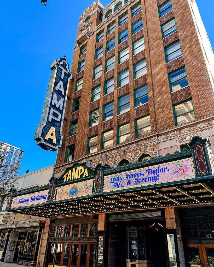 Iconic exterior of Tampa Theatre in Tampa Florida with its vintage marquee and bold vertical sign under a clear blue sky.