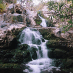 Long-exposure view of the multi-tier falls along the Copper Creek Falls and Mine trail, water streaming over green stone and boulders
