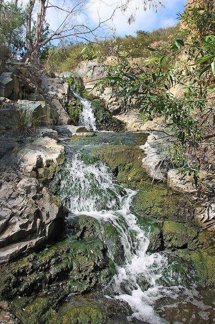 Small tiered waterfall spilling over moss-covered rocks beneath chaparral hills at Copper Creek Falls in Carlsbad, California