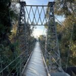 Spruce Street Bridge in San Diego surrounded by lush greenery, viewed from above with a pedestrian walking across.