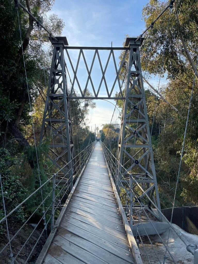 Spruce Street Bridge in San Diego surrounded by lush greenery, viewed from above with a pedestrian walking across.