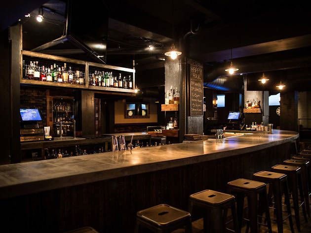 Interior of Blind Donkey Pasadena whiskey bar with long wooden counter, metal stools, shelves of spirits, and low-hanging pendant lights