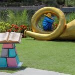 Boy Blue statue from Ulele Fairyland Figures Tampa crouched inside a giant golden horn beside an open storybook pedestal on the Riverwalk