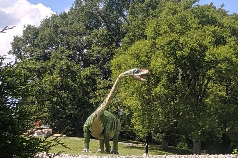 	Long-necked green dinosaur sculpture roaring beside oak trees at Boedecker Sculpture Garden, Nashville.