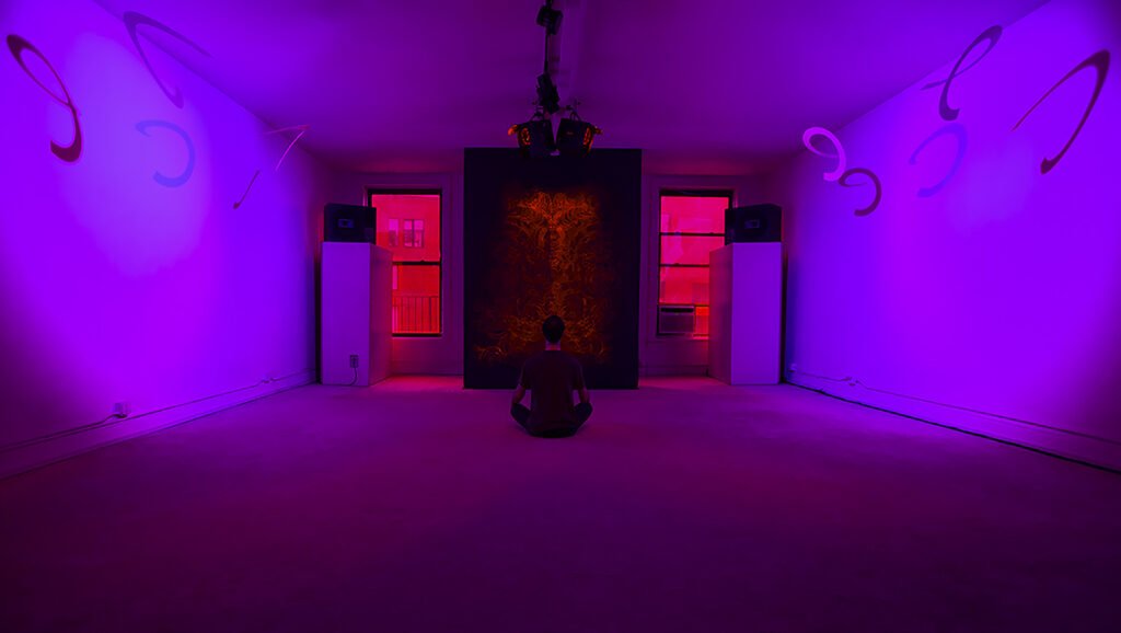 Visitor meditating inside Dream House New York City, violet light and orange fractal panel at center.