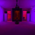 Visitor meditating inside Dream House New York City, violet light and orange fractal panel at center.