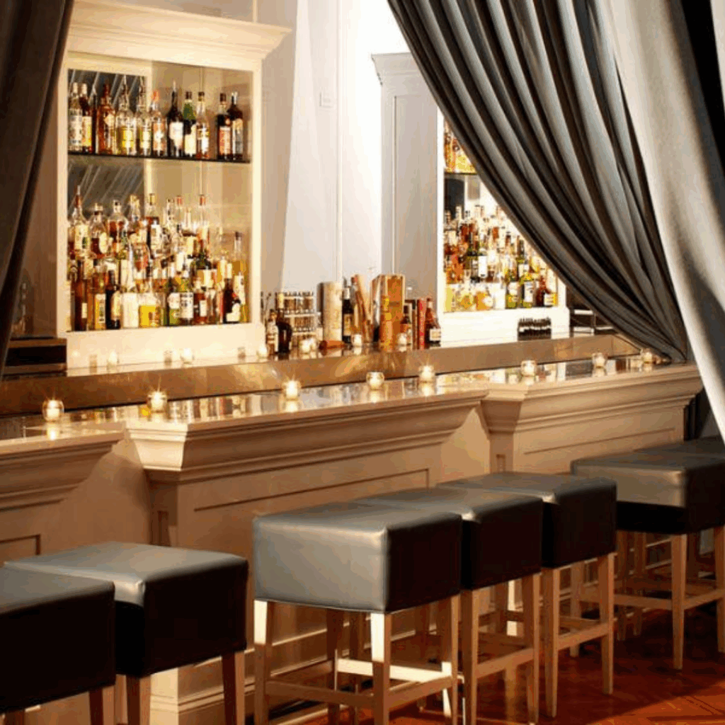 The Violet Hour Chicago candlelit bar interior with blue leather stools, marble counter, and velvet curtains framing shelves of spirits.