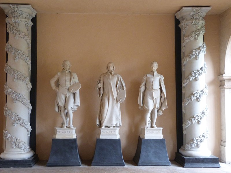 Three white marble statues of Velázquez, Murillo, and Zurbarán standing between decorative spiral columns in the Panama-California Sculpture Court, Balboa Park