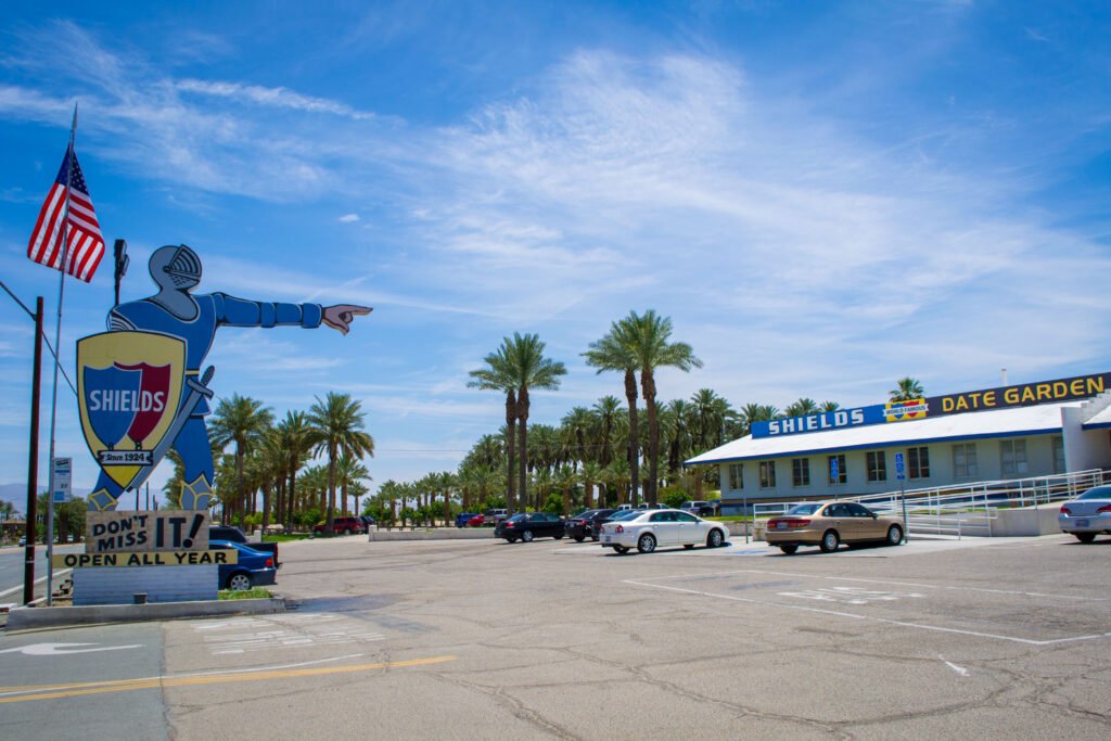 Iconic knight sign pointing toward Shields Date Garden Indio on Highway 111, with palm trees and a bright desert sky