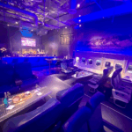 Angled view inside PS Air Bar Palm Springs with airplane seats, back-lit window walls, charcuterie on a wing table and bar.