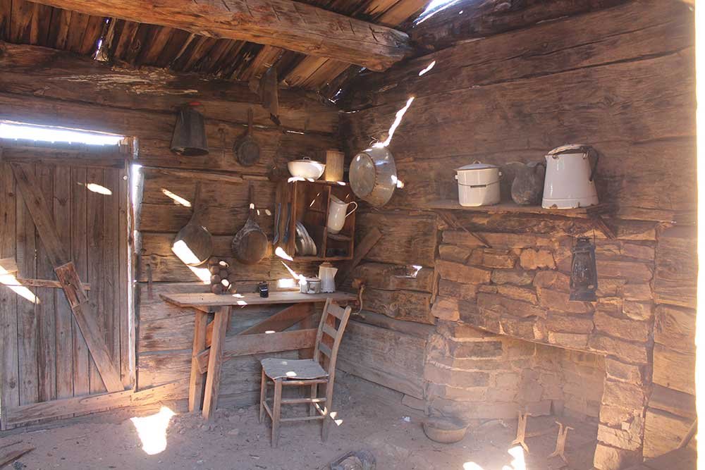 Inside Flying V Cabin Phoenix—rustic log walls, stone fireplace and vintage cookware lit by slivers of desert sun