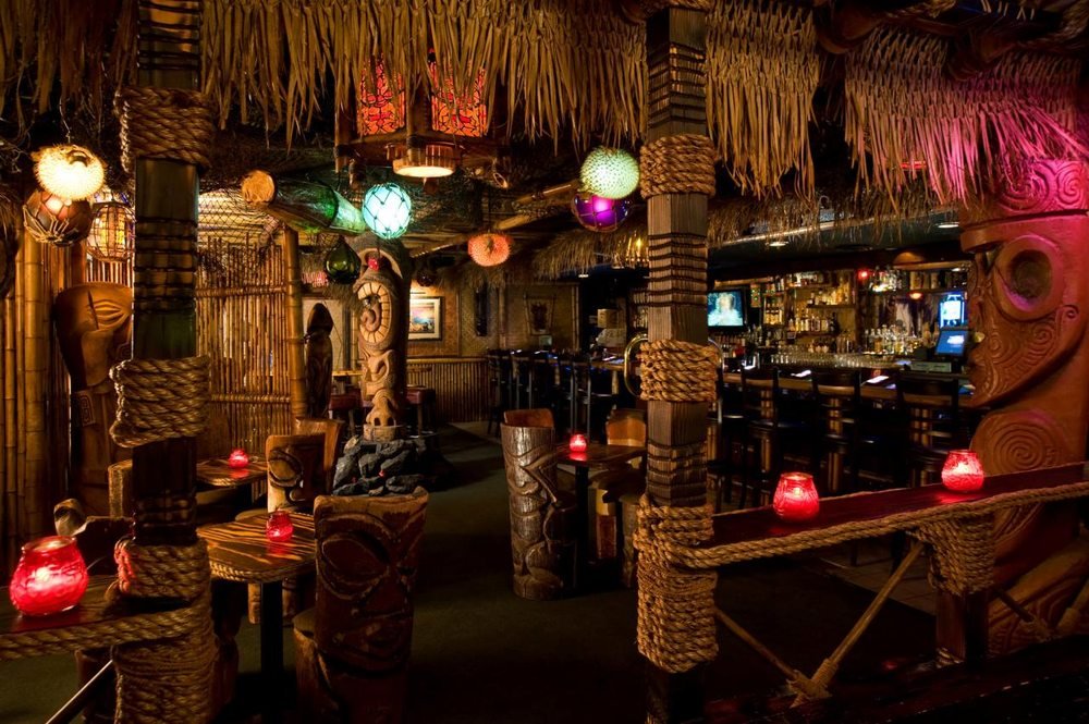 Interior of Frankie's Tiki Room showing bamboo pillars, tiki statues, hanging lanterns, and a cozy bar area