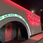 Exterior of Frankie's Tiki Room at night, featuring its bright neon sign and arched entrance