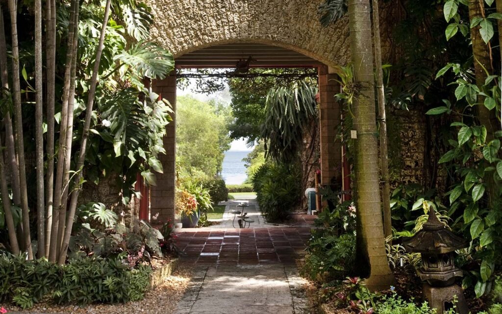Stone archway at The Kampong Miami opening onto Biscayne Bay, surrounded by lush tropical plants