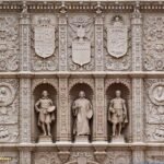 Ornately carved stone façade with relief shields, decorative motifs, and niches housing sculptures of Velázquez, Murillo, and Zurbarán at Balboa Park