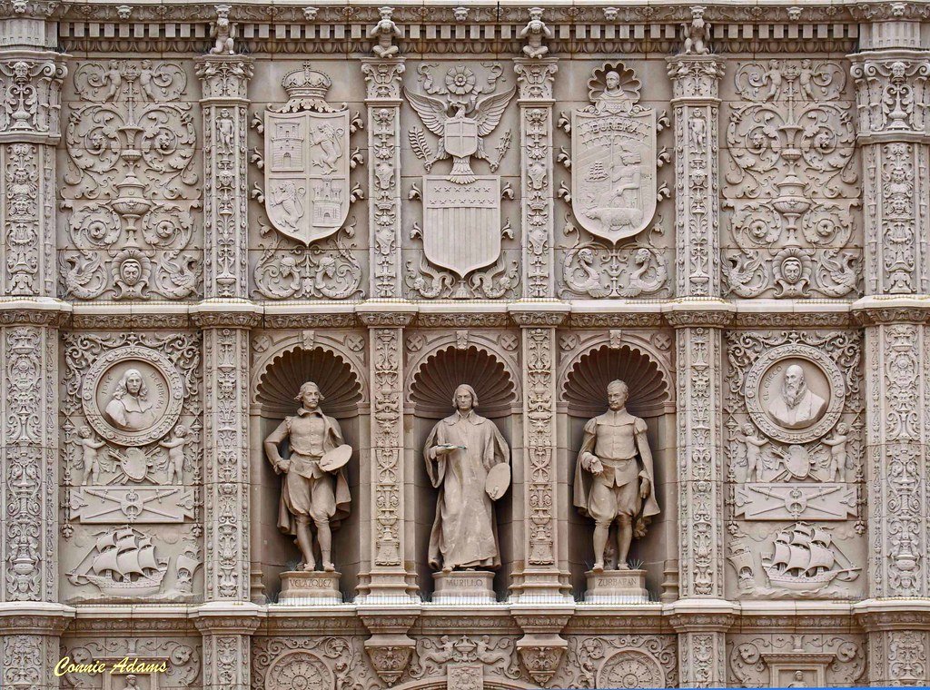 Ornately carved stone façade with relief shields, decorative motifs, and niches housing sculptures of Velázquez, Murillo, and Zurbarán at Balboa Park