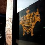 Blind Donkey Pasadena logo painted in orange on a glass window, featuring two donkey silhouettes and decorative lettering